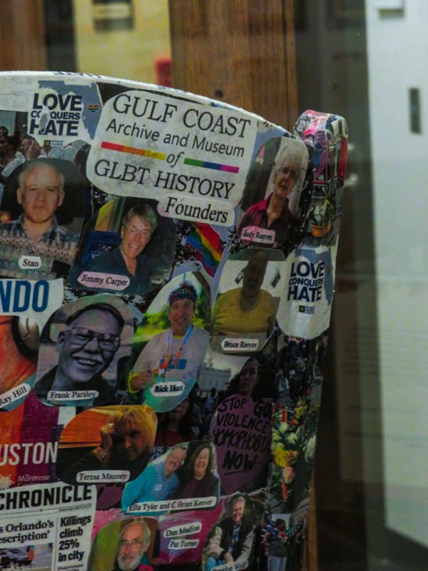 Detail of a chair covered by a collage of newspaper clippings, photos, images, and words, representing 47 years of LGBTQIA+ history and activism. The detail shows photos and text. Photos depict the founders of the Gulf Coast Archive and Museum of GLBT History, and the text spells out: “Gulf Coast Archive and Museum of GLBT History Founders.”