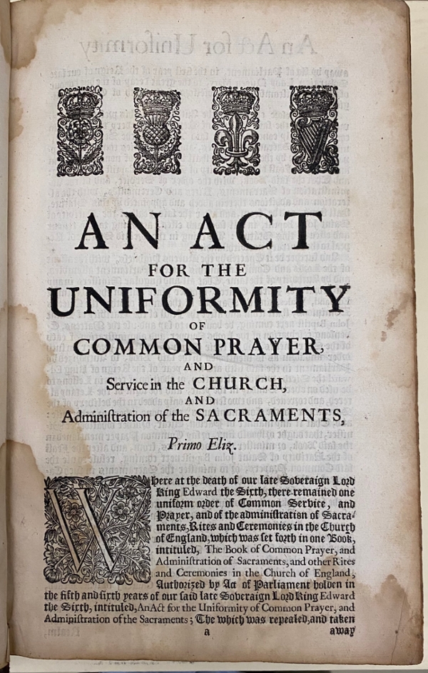 Original 1662 BCP, first page of the “Act for the Uniformity of Common Prayer.” There are black-and-white symbols at the top of the page, representing four countries: a rose for England, a thistle for Scotland, a fleur-de-lis for France, and a harp for Ireland. The first letter in the page text is an ornate upper-case “W”. The book is held at the Cushing Memorial Library and Archives.